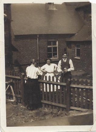 An unusual view of the back of the School room, soon after it was built in 1914. The people in the photo may be the caretakers who lived in the Chapel Cottage next door. This would be the side of the fence in the foreground.